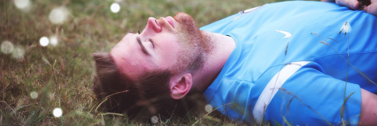 Can a Real Man Have Anxiety man with beard lying on back in field with eyes closed