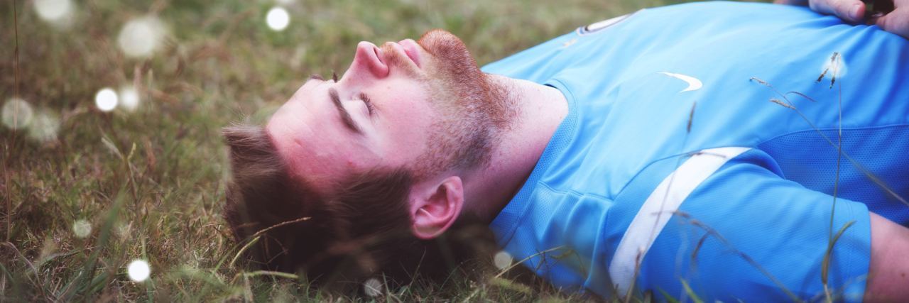 man with beard lying on back in field with eyes closed