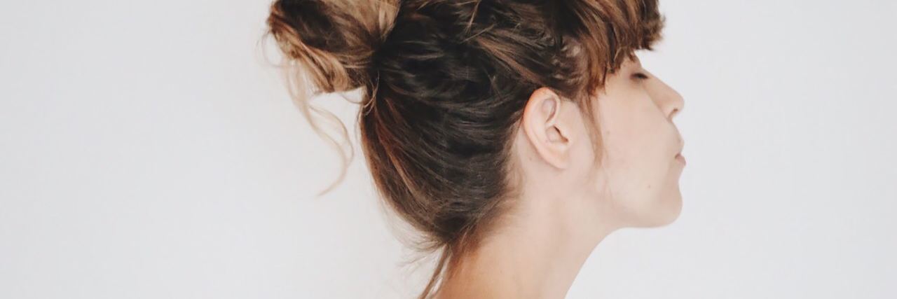 Why Endometriosis Is Not 'Just a Bad Period' woman wearing a white shirt standing against a white wall looking up with her eyes closed