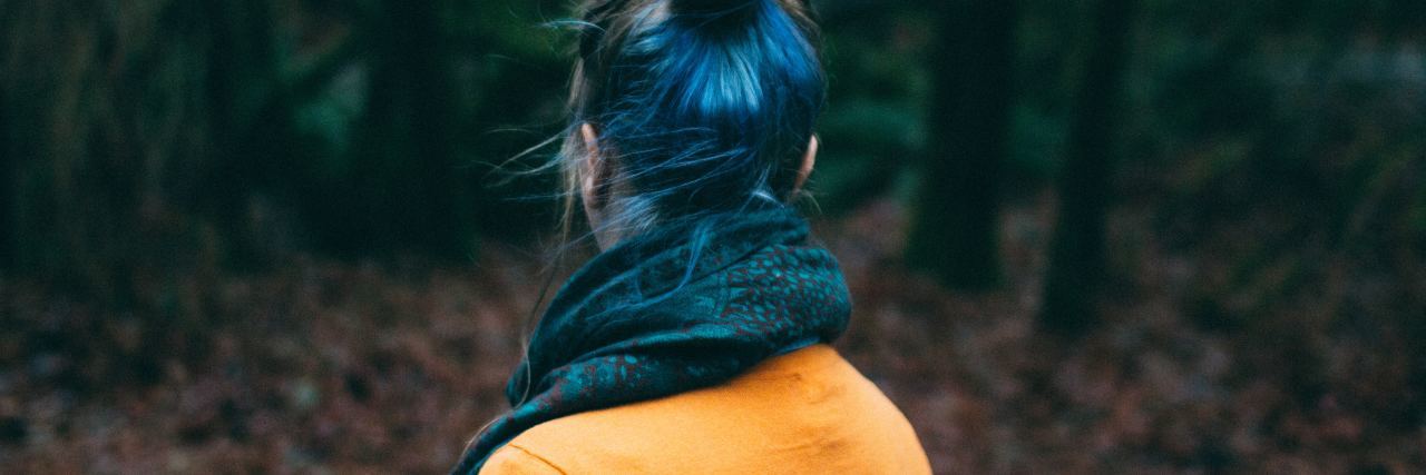 woman with blue hair facing away and looking into woods