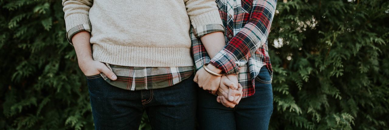 close up of couple wearing plaid shirts holding hands in front of hedge