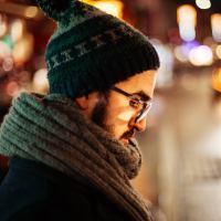 man with beard and glasses standing on street at night looking down and tired