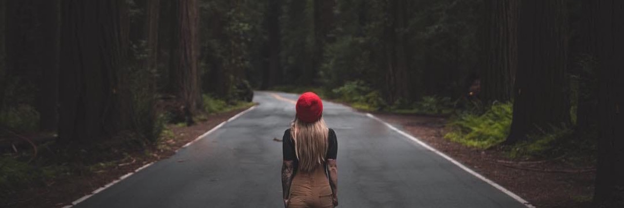 woman walking down the middle of the road in a forest