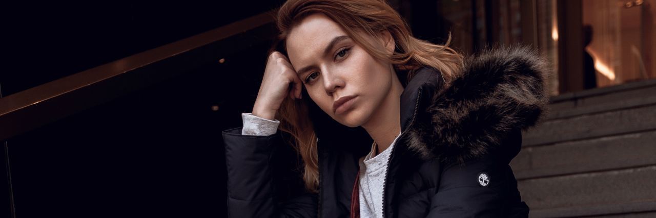 Common Misconceptions About Fibromyalgia – and the Truth woman sitting on concrete stairs and wearing a black puffy jacket