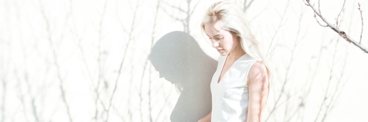 What to Ask Your New Dissociative Identity Disorder Therapist blonde woman standing in front of white wall with shadows of tree branches