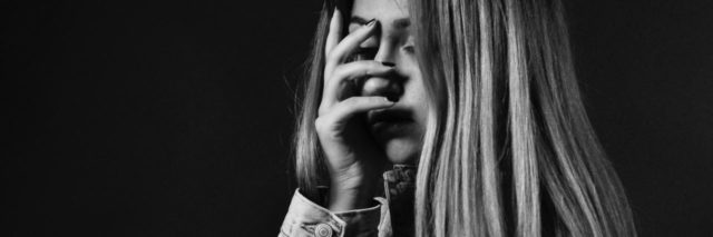 black and white photo of young blonde teen covering face with hand and eyes closed