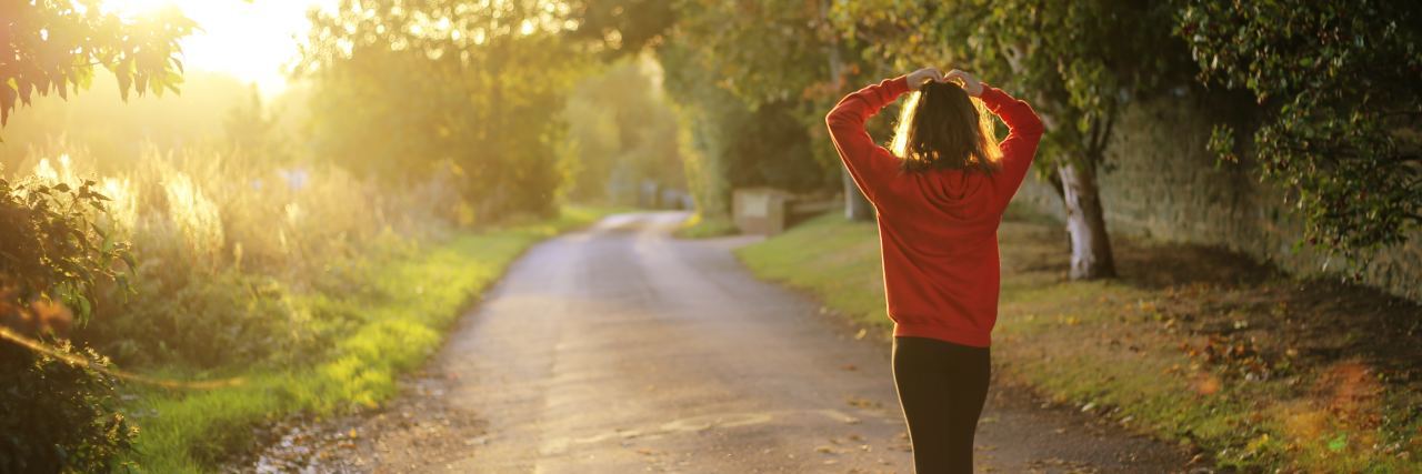 woman in red sweater walking along country road with trees and hedges