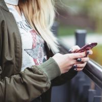 close up of young blonde woman scrolling through her phone by railing and park