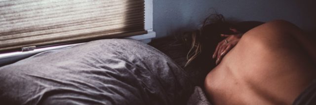 woman lying in bed beside window asleep and facing away