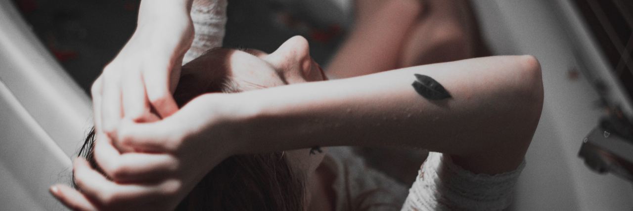 How to Cope With an Emotional Hangover overhead view of woman sitting in bath with arms raised to her head