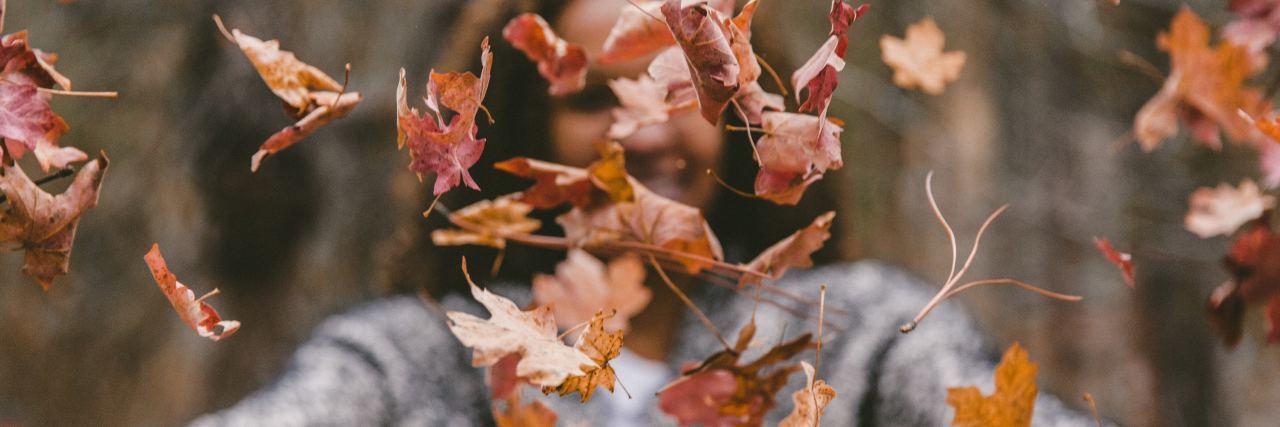 Why I'm Thankful This Thanksgiving as a Person With Chronic Illness woman throwing autumn leaves