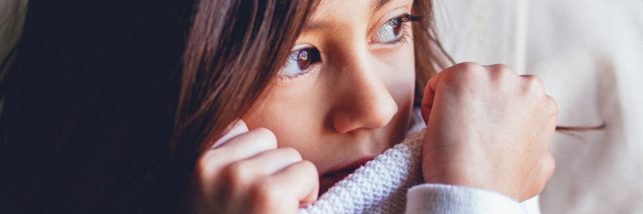 What to Say and Not Say to a Child With Depression young girl looking upset with sweater pulled up to cover mouth