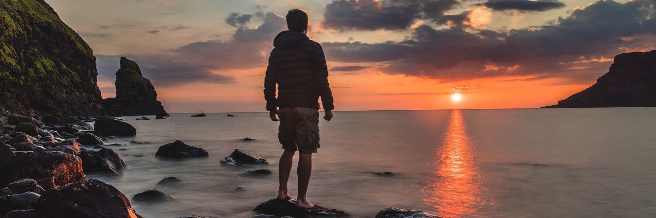 man standing on rocks in water watching sunrise over ocean