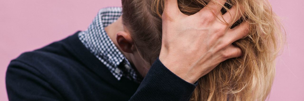 How to Support Your Non-Binary Family During the Holidays non binary person with long blonde hair and hidden face holding head in hand