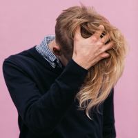 non binary person with long blonde hair and hidden face holding head in hand