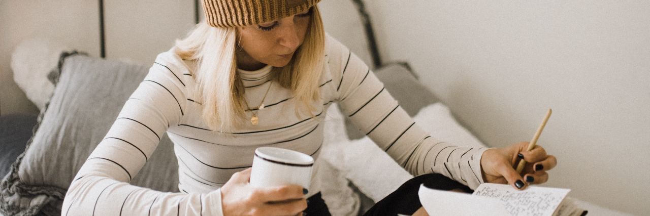 Benefits of Self-Monitoring in Addiction Recovery woman sitting on bed with coffee cup and notebook writing