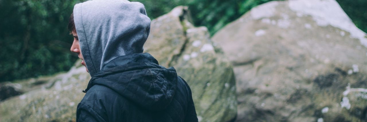 young man standing outside on rocks with hood covering back of head