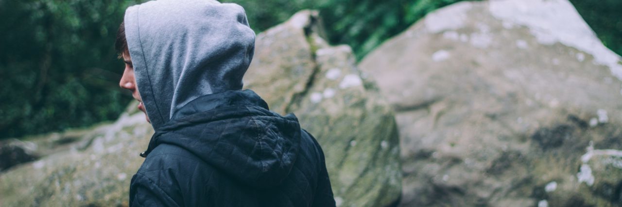 Teen Anger as a Sign of My Borderline Personality Disorder young man standing outside on rocks with hood covering back of head