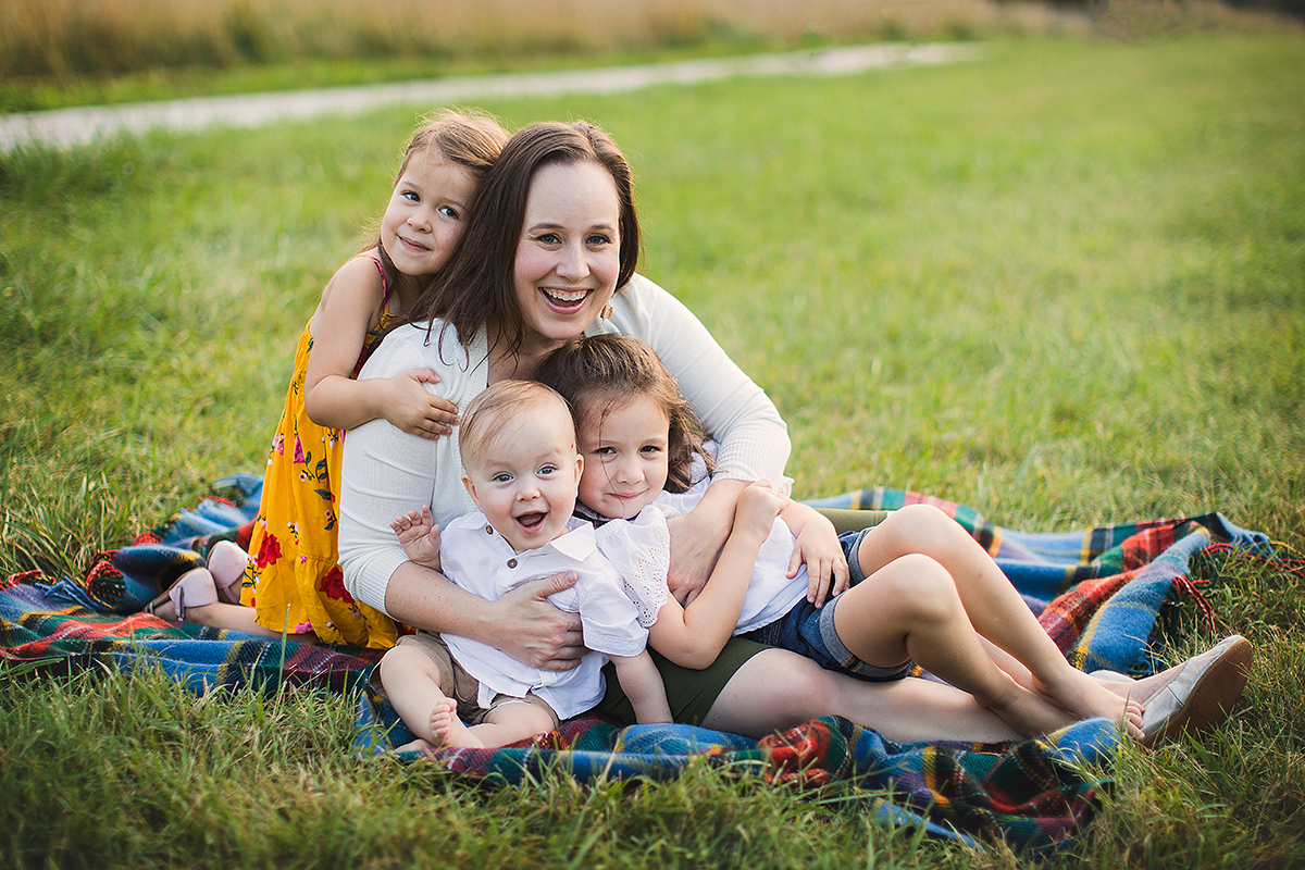 Owen with his mom and sisters all sitting on a blanket in the grass.