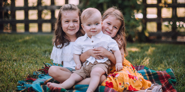 Owen with his two sisters sitting in the grass.