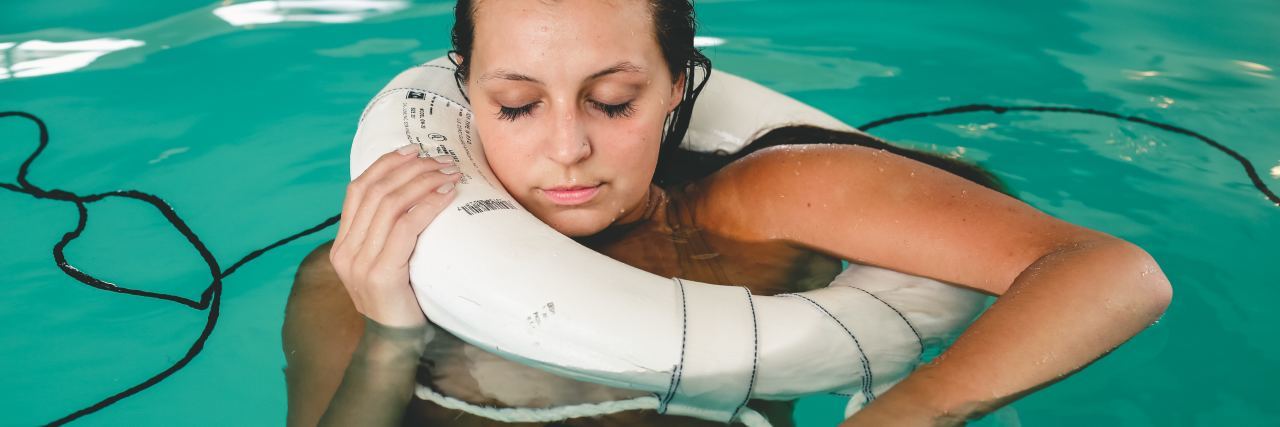 woman holding on to life ring in swimming pool with eyes closed