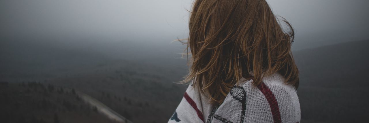 Hidden Effects of Self-Harm woman wrapped in blanket looking out over misty countryside