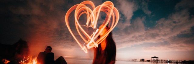 woman sitting on beach making heart shape in air with light