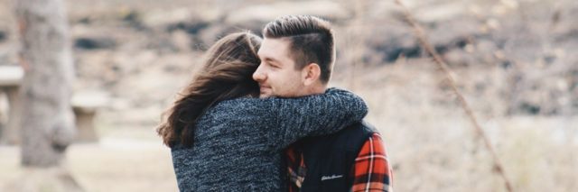 man and woman hugging outdoors with woman's face hidden in man's shoulder