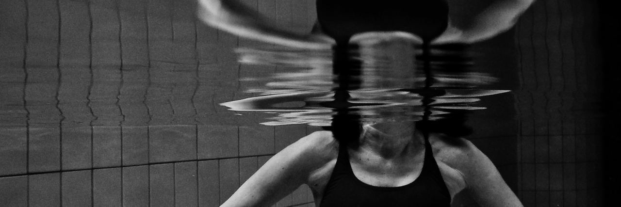 black and white photo of woman doubled by reflection in pool underwater