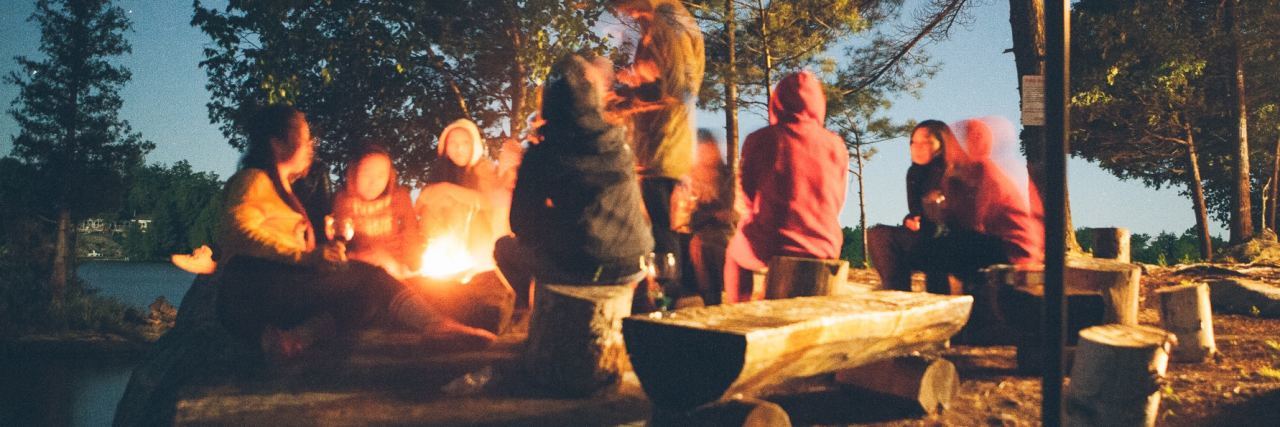 group of young people around campfire at night
