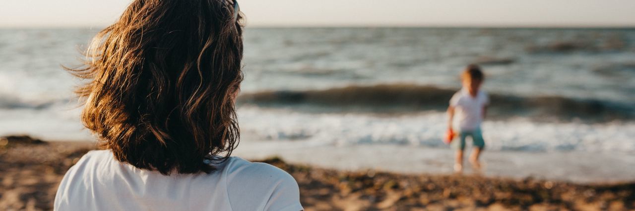 Self-Harm as a Parent woman watching son play on beach in soft focus