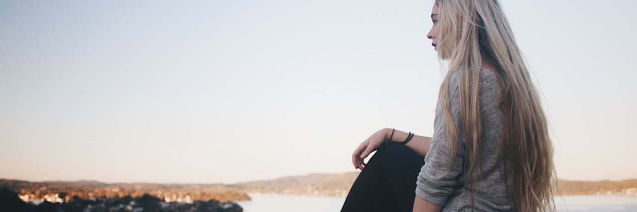 Why Anxiety Is More Than Stress young blonde woman sitting on edge of pier or viewpoint looking out over water and mountains