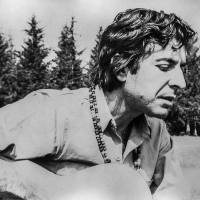 old black and white photo of Leonard Cohen playing guitar