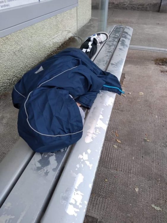 young boy lying on bench covered in coat