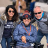 Image of mother and father on each side of adult son who is sitting on his wheelchair. All three are smiling at the camera.