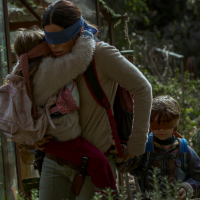 Sandra Bullock holding a young girl and the hand of a young boy while all are blindfolded running through a forest.
