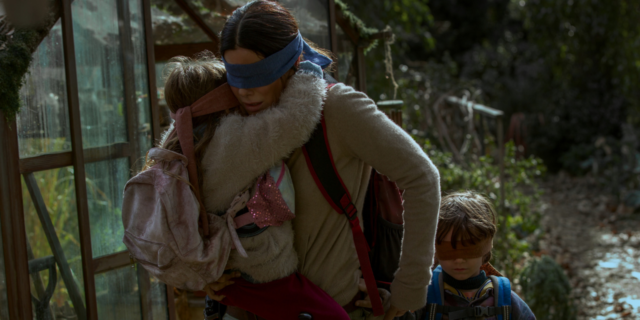 Sandra Bullock holding a young girl and the hand of a young boy while all are blindfolded running through a forest.