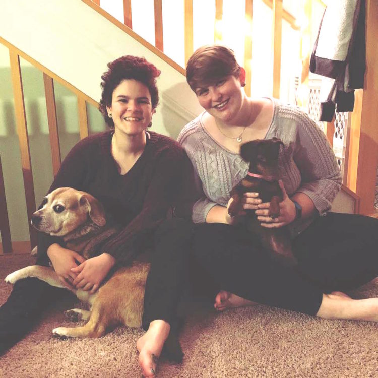 lesbian couple posing with two dogs in front of staircase