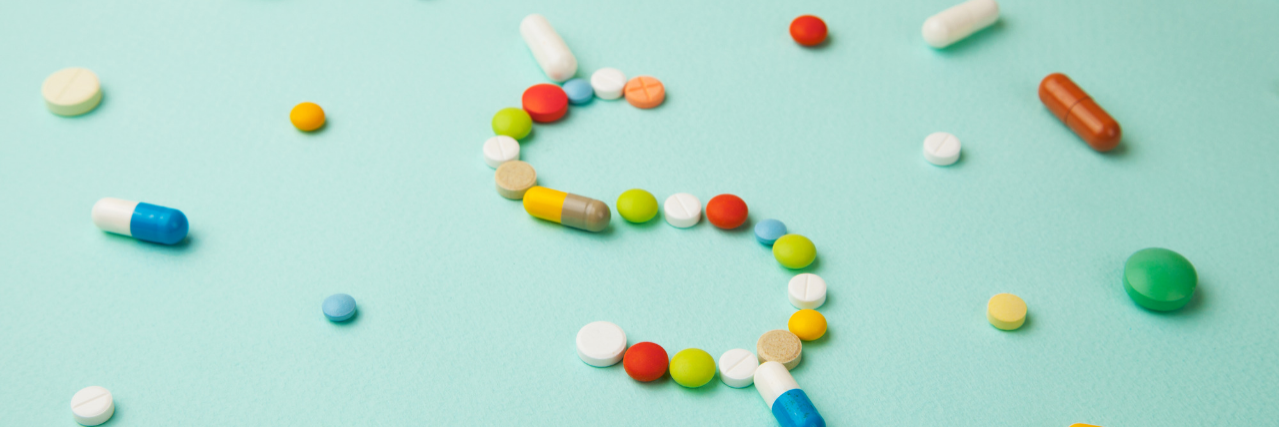 CMS Hospital Transparency Mandate Shows Prices Online Light blue background with different pills scattered. In the middle, some pills make a dollar sign.