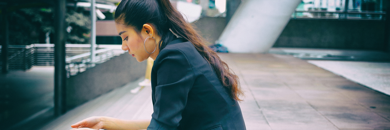 Stressed young Asian woman sitting on stairs.