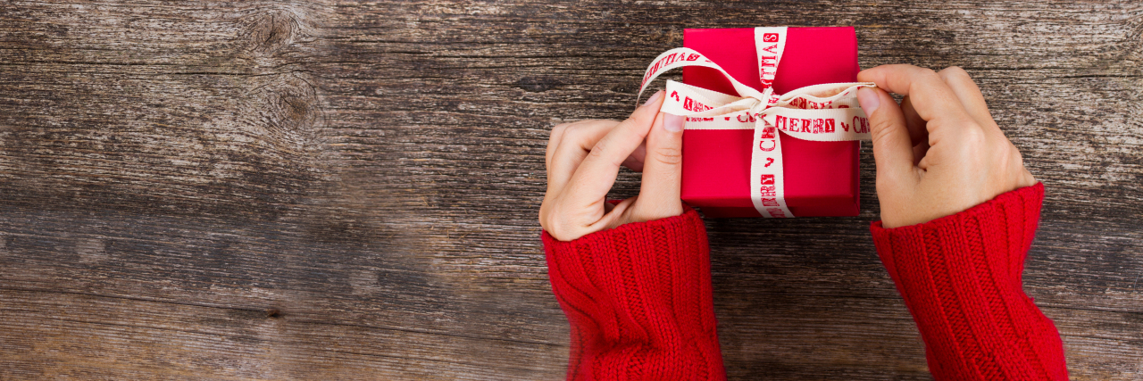 Mental Health Inspired Holiday Gifts A woman's hands holding a red holiday gift box