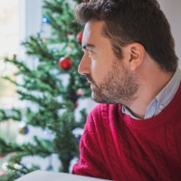 man wearing a red sweater and sitting in front of a christmas tree