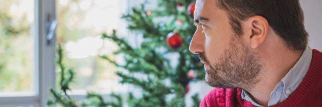 man wearing a red sweater and sitting in front of a christmas tree