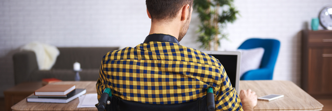 The Challenge of Receiving Benefits and Working With a Disability Disabled man in wheelchair using laptop computer.