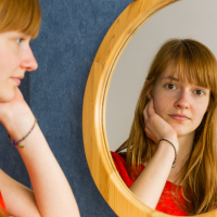 Red haired young woman looking at herself in the mirror.