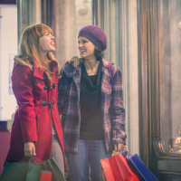 two women wearing coats and walking down the street carrying shopping bags