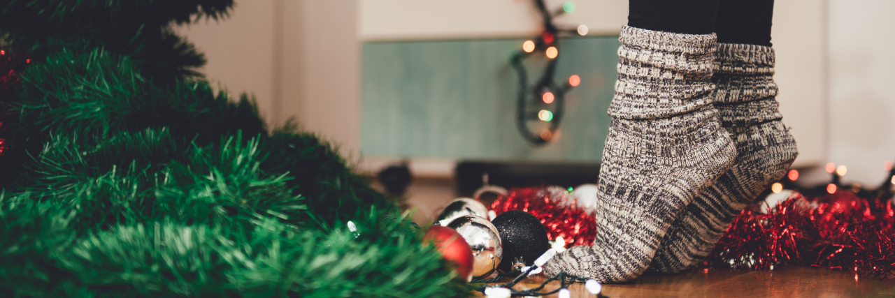 How to Prepare for Next Christmas If You Have a Chronic Illness woman wearing cozy socks and standing on her tiptoes to decorate her christmas tree