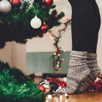 woman wearing cozy socks and standing on her tiptoes to decorate her christmas tree