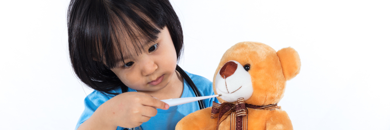Little girl playing doctor with a teddy bear.