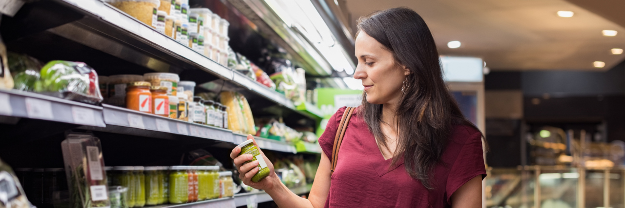 Why I'm Not Changing My Diet to Help With My Autoimmune Disease woman shopping at the grocery store and holding up a jar of something to read